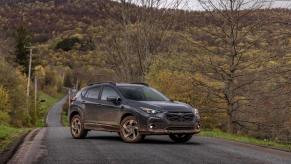 A 2024 Subaru Crosstrek compact SUV model caked in dirt and parked in the middle of a road near a yellow forest