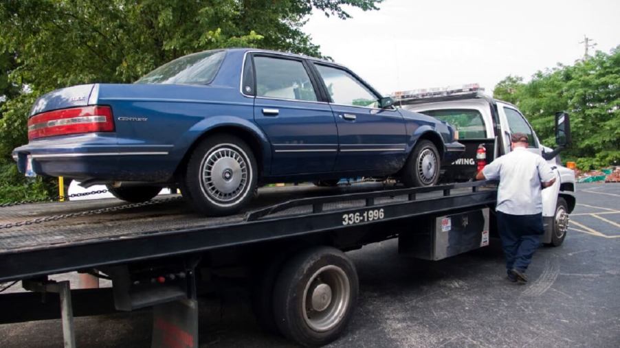 A AAA flat bed towing truck provides roadside assistance to a broken-down car.