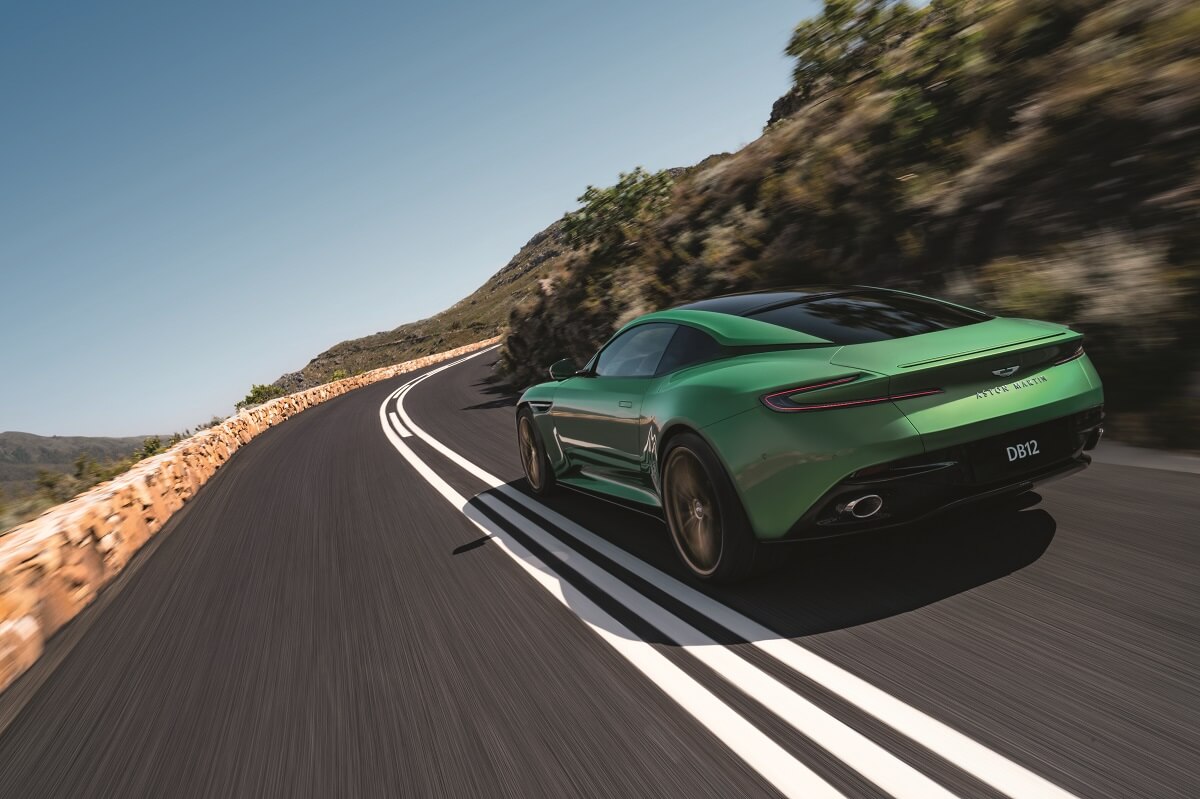 An Aston Martin DB12 flexes its grand tourer muscle by cornering on a mountain pass.