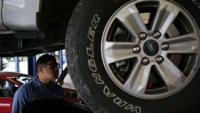 A car mechanic inspects the underside of a car to see if the axles are okay.