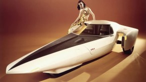 A model sits on the fender of a futuristic, rocket-shaped 1969 Chevrolet prototype at an auto show.