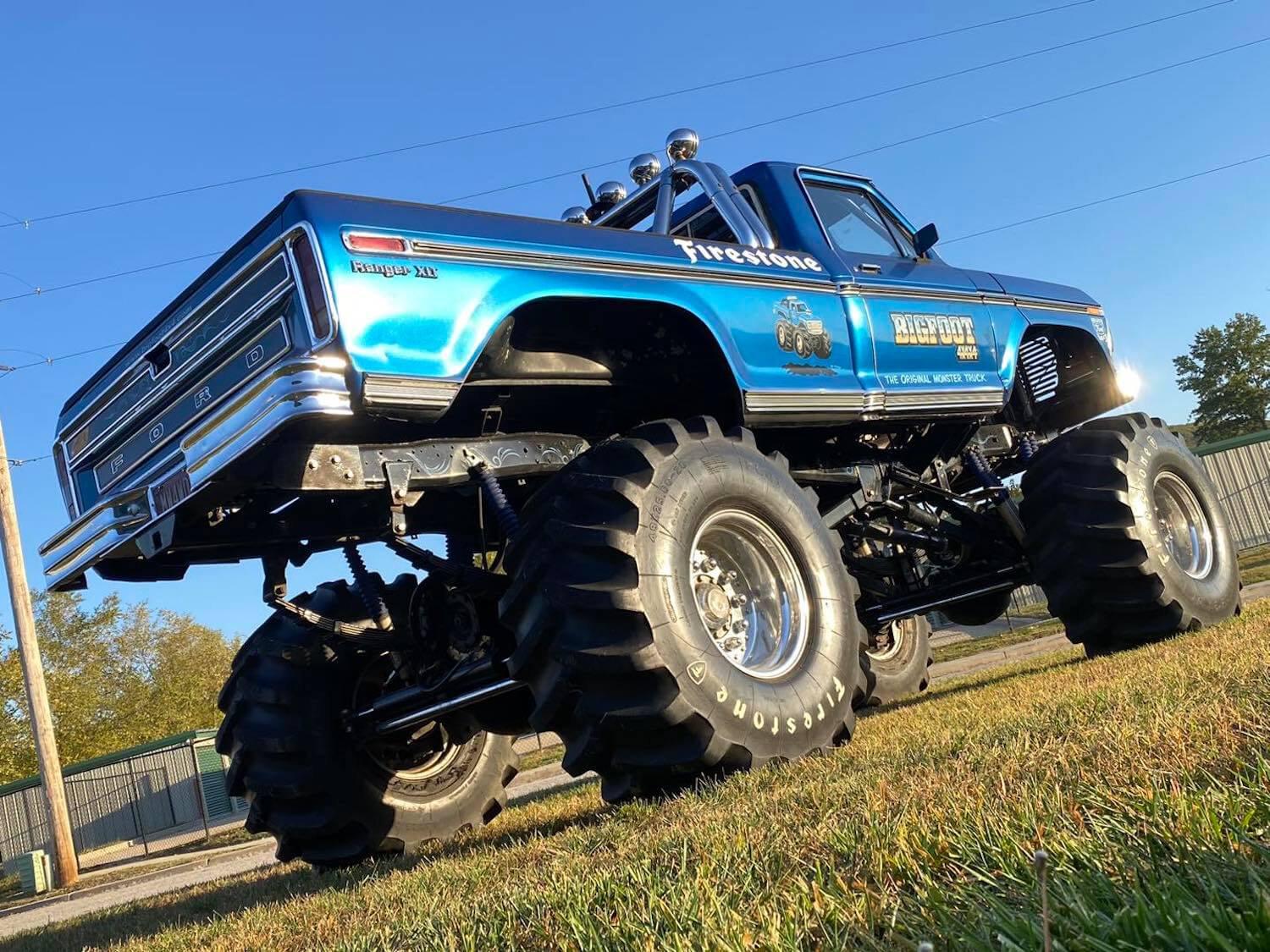 Closeup of the tailgate and rear tires of an early Bigfoot Ford F-250 monster truck parked on grass.