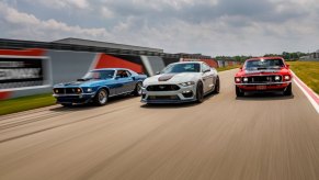 A series of Ford Mustang Mach 1 models cruise down a race track.