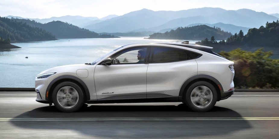 A white 2023 Ford Mustang Mach-E small electric SUV is driving on the road. 