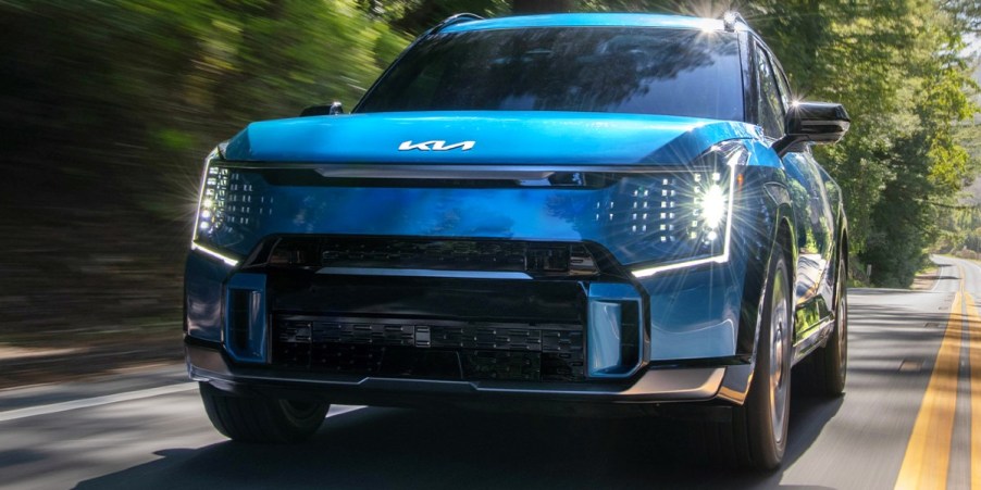 A blue 2023 Kia EV9 midsize electric SUV is driving on the road.