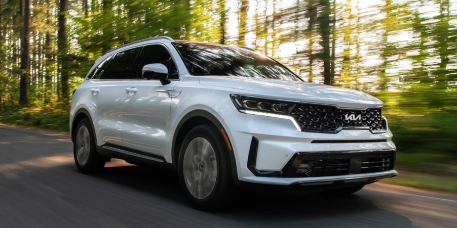 A white 2023 Kia Sorento Plug-In Hybrid midsize SUV is driving on the road.