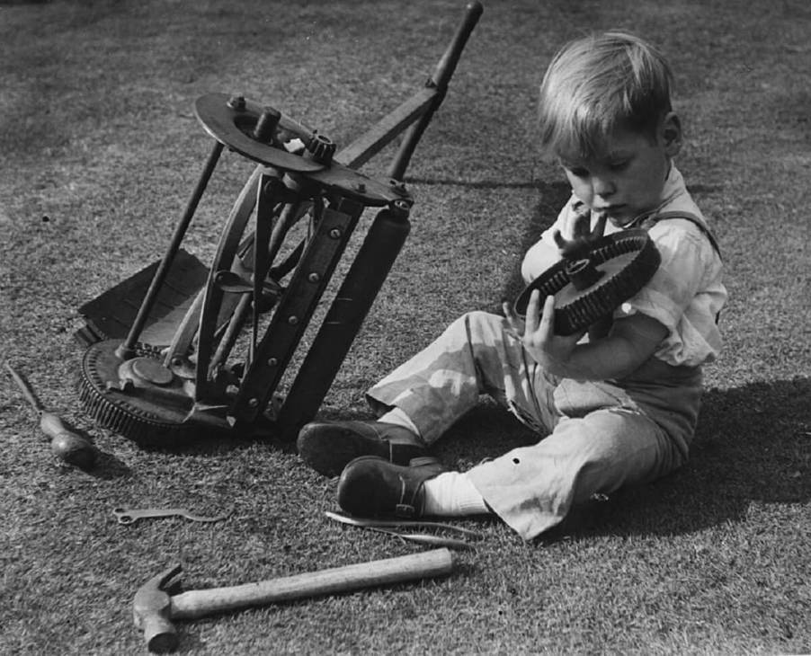 A young boy rolls over a lawn mower and repairs it.