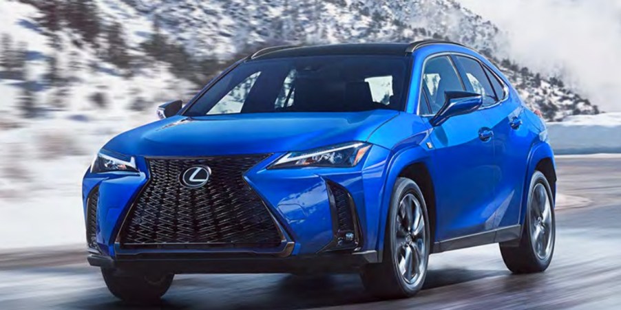 A blue 2023 Lexus UX subcompact luxury SUV is driving on the road.