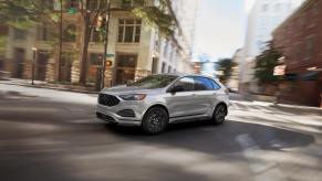 A silver 2023 Ford Edge drives through a city.