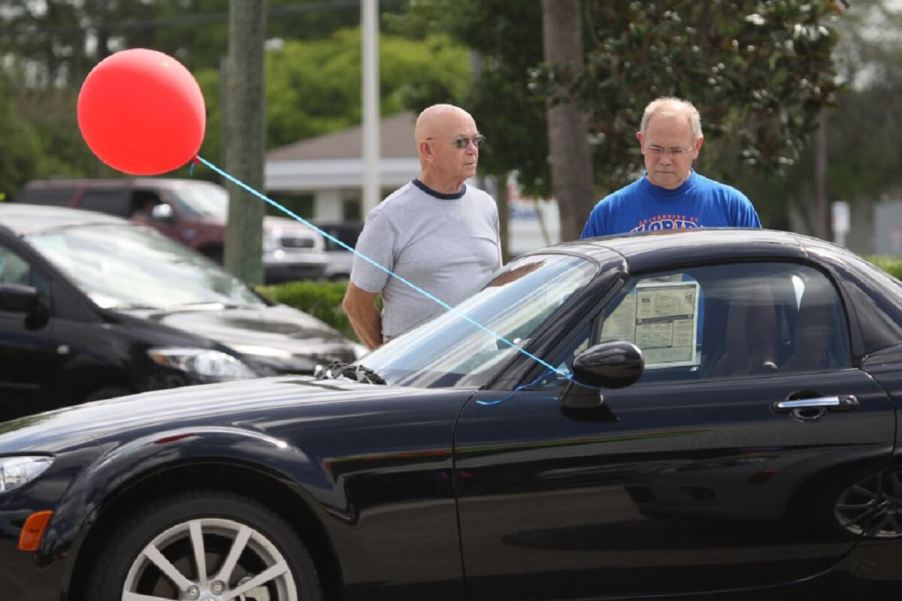 Two older potential owners inspect a Mazda MX-5 Miata.