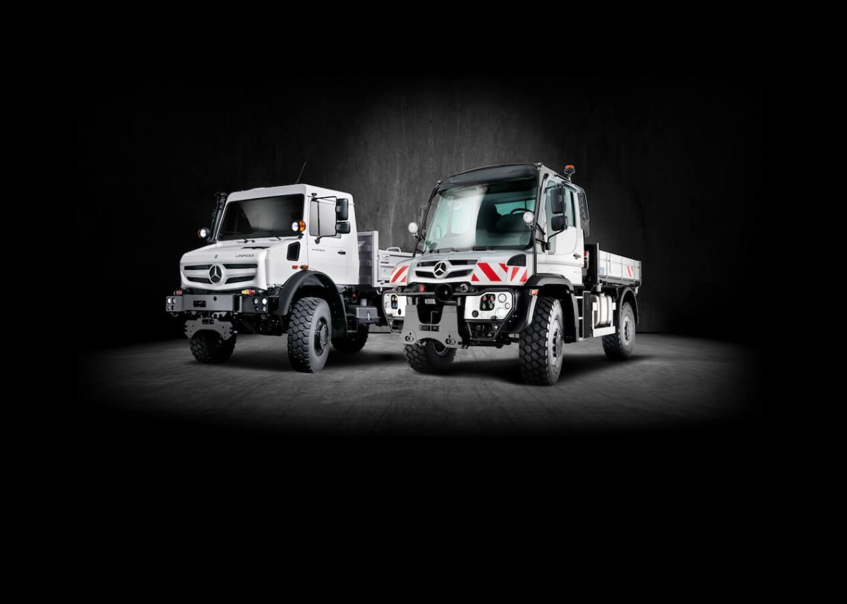 White Mercedes-Benz Unimog models spotlighted against a black background.