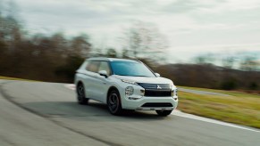 A white 2023 Mitsubishi Outlander PHEV, a great plug-in hybrid SUV for families, drives vigorously.