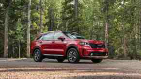 A red 2023 Kia Sorento sits amid a green forest. It's the most efficient none-electric, non-plug-in midsize SUV of 2023.