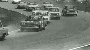 A black and white photo of a Nissan Skyline GT on a racetrack, which is powered by a Gloria V6 engine