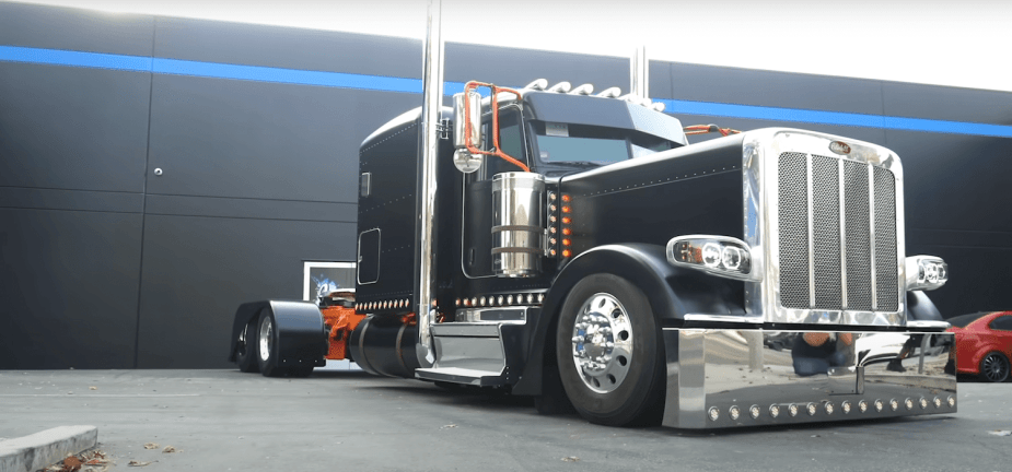 A black Peterbilt Semi-truck customized with chrome, parked in front of a black wall.