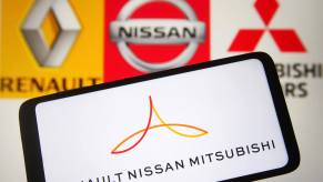 Cellphone with the Renault-Nissan-Mitsubishi Alliance logo with Renault, Nissan, and Mitsubishi's individual logos visible in the background.