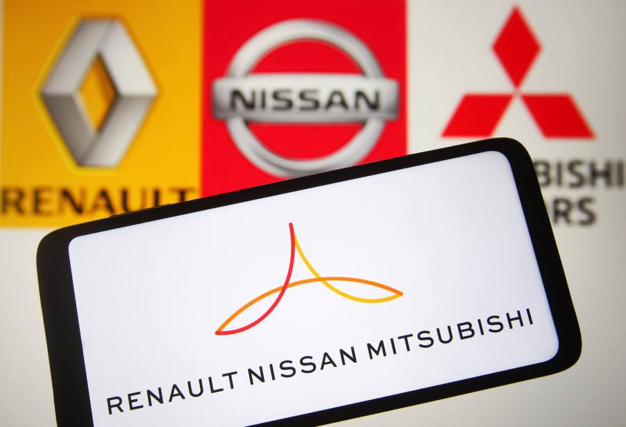 Cellphone with the Renault-Nissan-Mitsubishi Alliance logo with Renault, Nissan, and Mitsubishi's individual logos visible in the background.