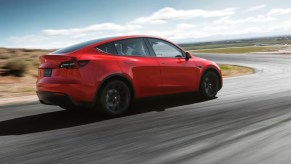 A red 2023 Tesla Model Y small electric SUV is driving on the road.