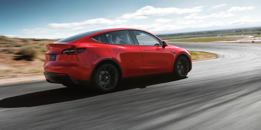 A red 2023 Tesla Model Y small electric SUV is driving on the road.