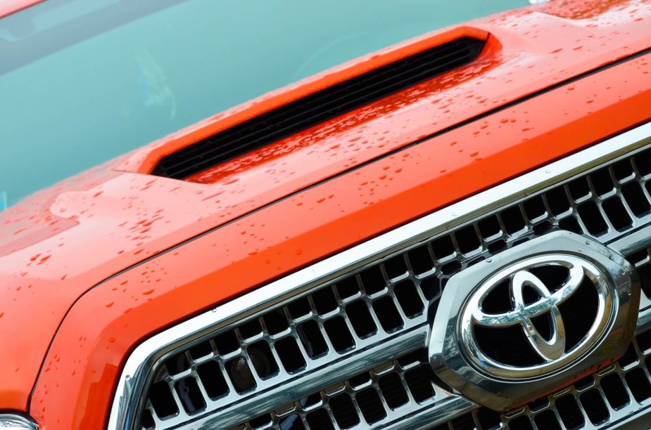 Closeup of the Toyota badge in the grille of an orange pickup truck.