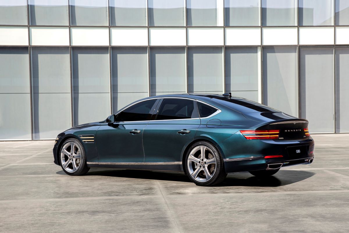 A side rear profile shot of a blue-green Genesis G80 executive sedan/luxury car model