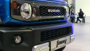 A blue Suzuki Jimny off-road SUV model on display with make and model nameplate front badging