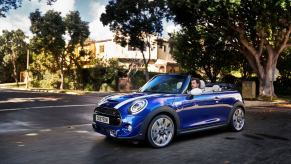 A blue and white 2019 Mini Convertible compact car driving through an intersection in a suburb