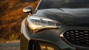 A zoomed in shot of a gray 2023 Kia Stinger sports sedan model features its grille, headlight, and side mirror