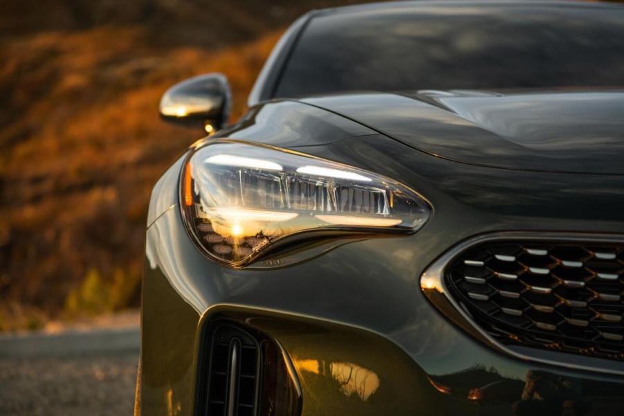 A zoomed in shot of a gray 2023 Kia Stinger sports sedan model features its grille, headlight, and side mirror