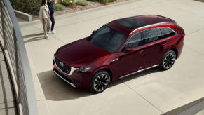 An overhead shot of a red 2024 Mazda CX-90 full-size SUV model with a couple walking toward it