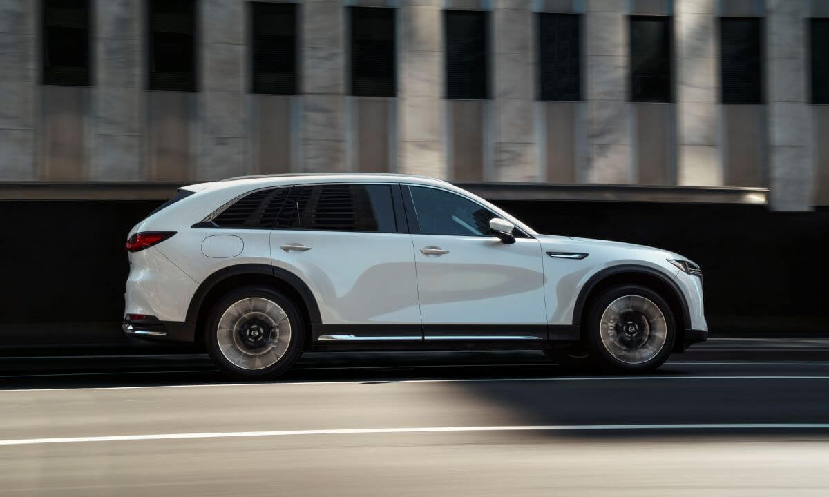 An exterior side shot of a white 2024 Mazda CX-90 PHEV full-size SUV model driving