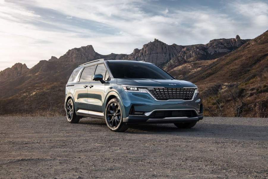 A fully loaded 2024 Kia Carnival minivan parked on gravel in front of mountains