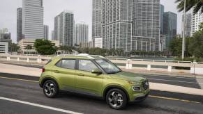 A bright green 2023 Hyundai Venue subcompact SUV model parked on a highway overpass with skyscrapers behind it