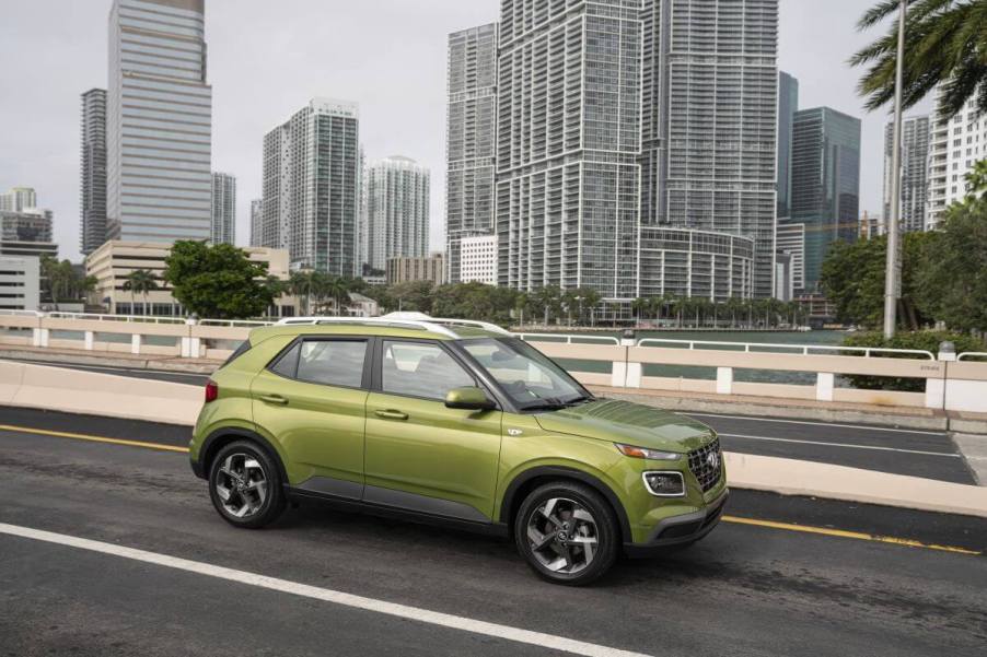 A bright green 2023 Hyundai Venue subcompact SUV model parked on a highway overpass with skyscrapers behind it