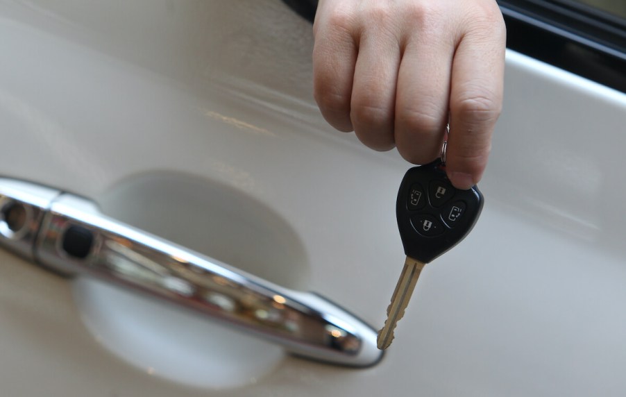 A man's hand holds a car key out a car door window.