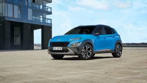 A blue 2023 Hyundai Kona located outside a modern building with blue skies in the background.