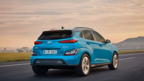 The rear of a blue 2023 Hyundai Kona Electric driving into the sunset