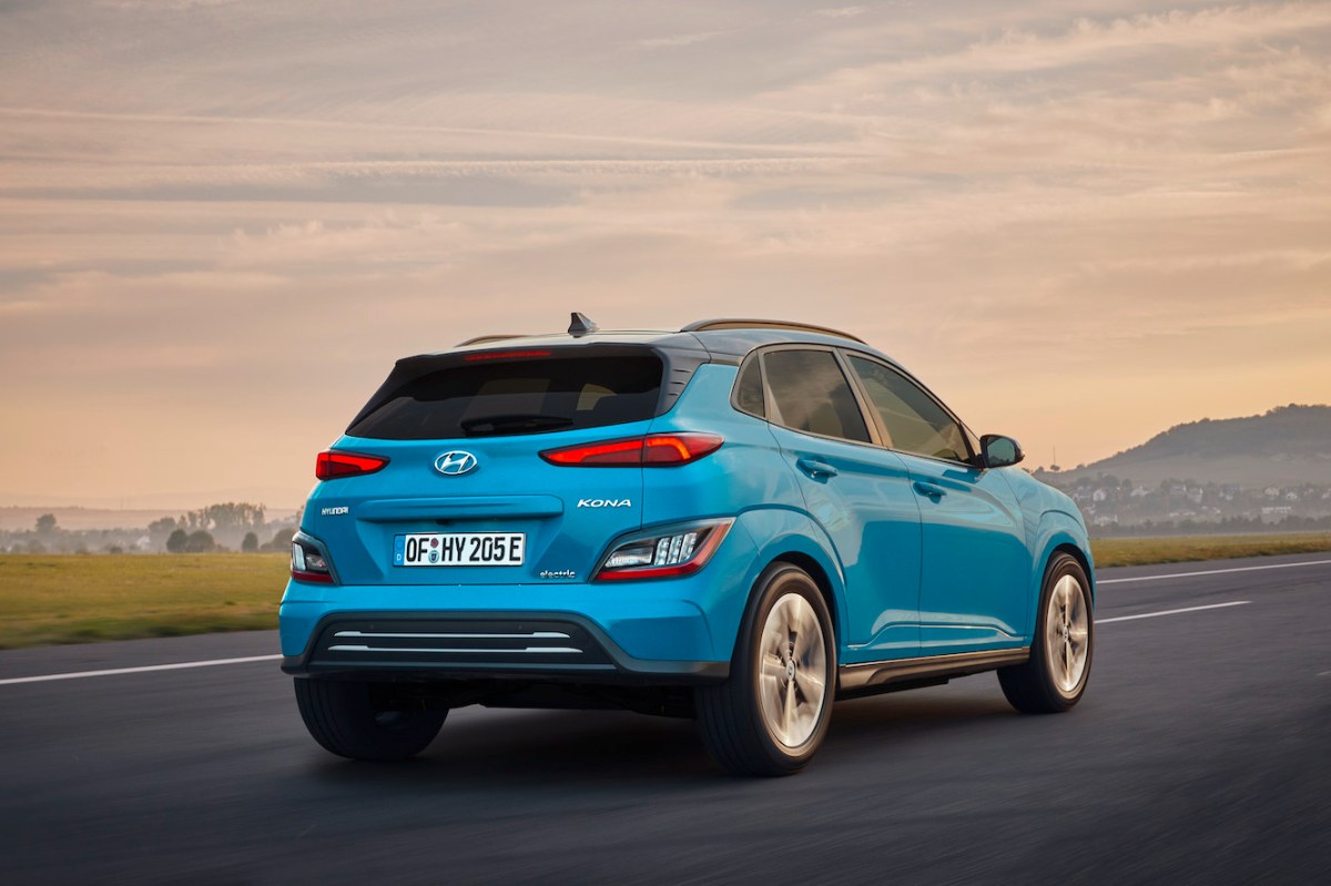 The rear of a blue 2023 Hyundai Kona Electric driving into the sunset