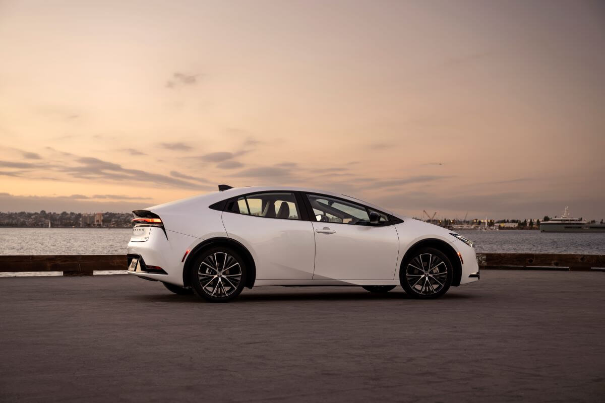 A side profile shot of a 2023 Toyota Prius hybrid hatchback model in Wind Chill Pearl parked by the sea