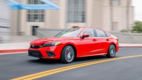 A bright red 2023 Honda Civic compact sedan model speeding past a building entrance with a blurred background