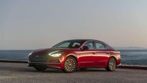 A red 2023 Hyundai Sonata Hybrid midsize sedan model with its headlights on parked on beach sand