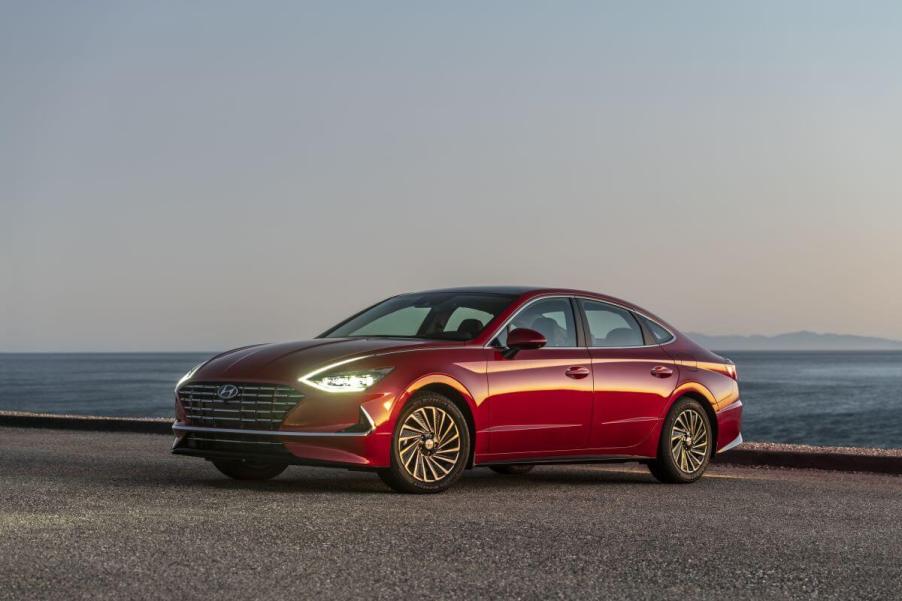 A red 2023 Hyundai Sonata Hybrid midsize sedan model with its headlights on parked on beach sand