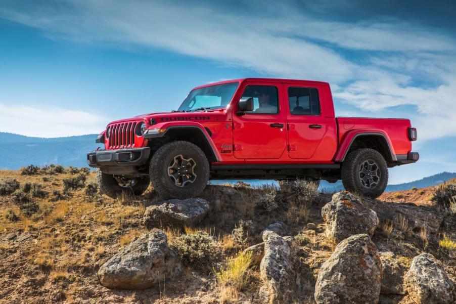 A red 2023 Jeep Gladiator Rubicon midsize pickup truck model perched on a grassy hill surrounded by large rocks