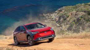 A red 2023 Subaru Solterra EV with AWD driving up a sand and gravel hill as it kicks up dust.