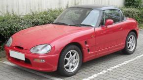 A red Suzuki Cappuccino subcompact sports car convertible coupe model parked on a cobblestone road