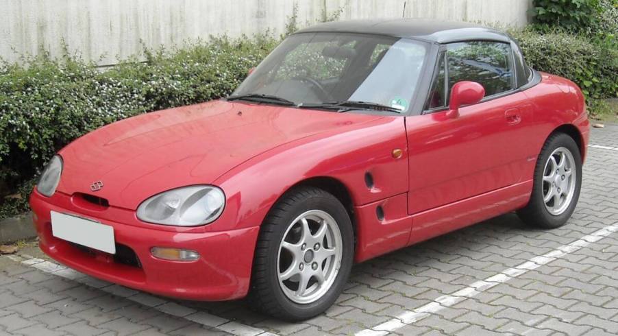 A red Suzuki Cappuccino subcompact sports car convertible coupe model parked on a cobblestone road