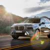 A gray 2023 BMW X7 on the road with a mountain and the sun in the background