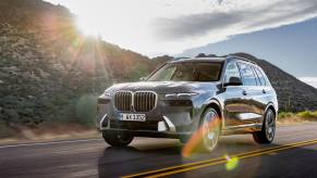 A gray 2023 BMW X7 on the road with a mountain and the sun in the background