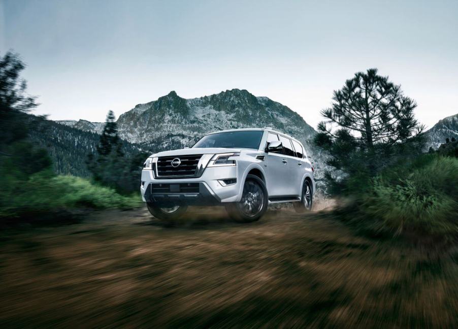 A white 2023 Nissan Armada full-size SUV driving on a dirt forest path with a snowy mountain in the background