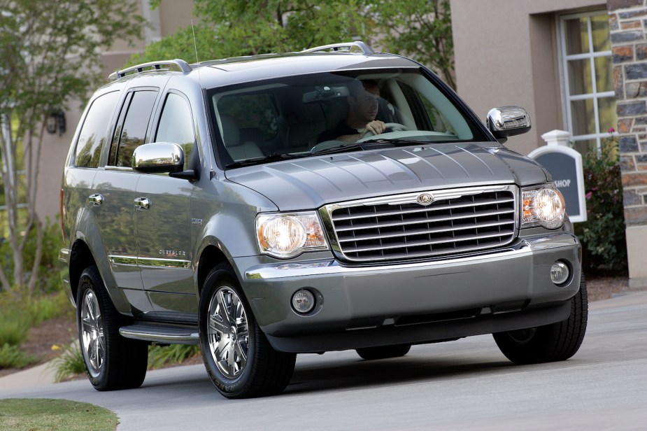 A silver Chrysler Aspen SUV parked in front of a house.